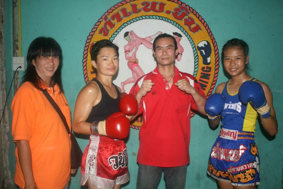 Kru Roen posing with fighters in front of the gym logo, years ago